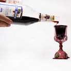 Person pouring grape wine from a bottle into a kiddush cup pipe on a white background