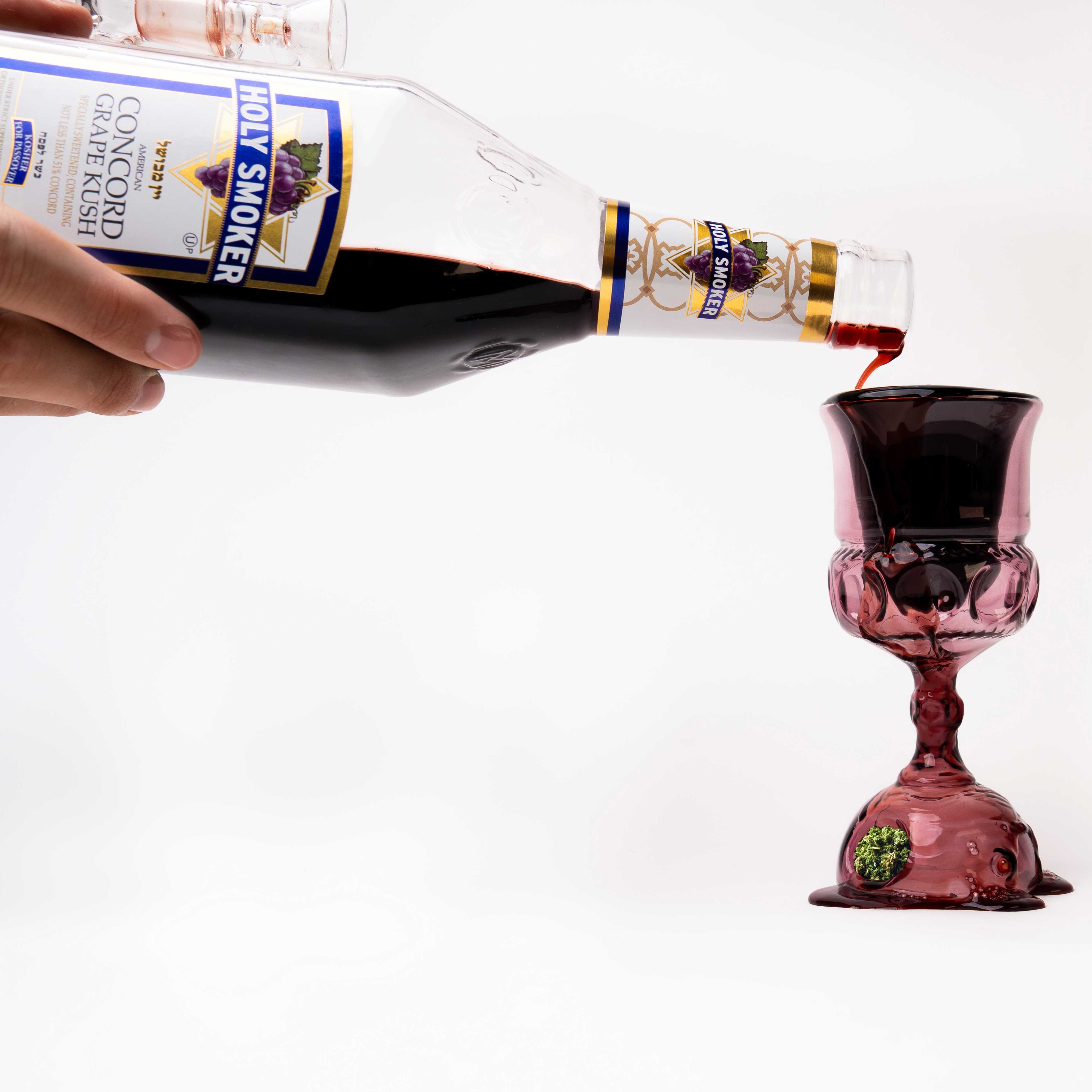 Person pouring grape wine from a bottle into a kiddush cup pipe on a white background
