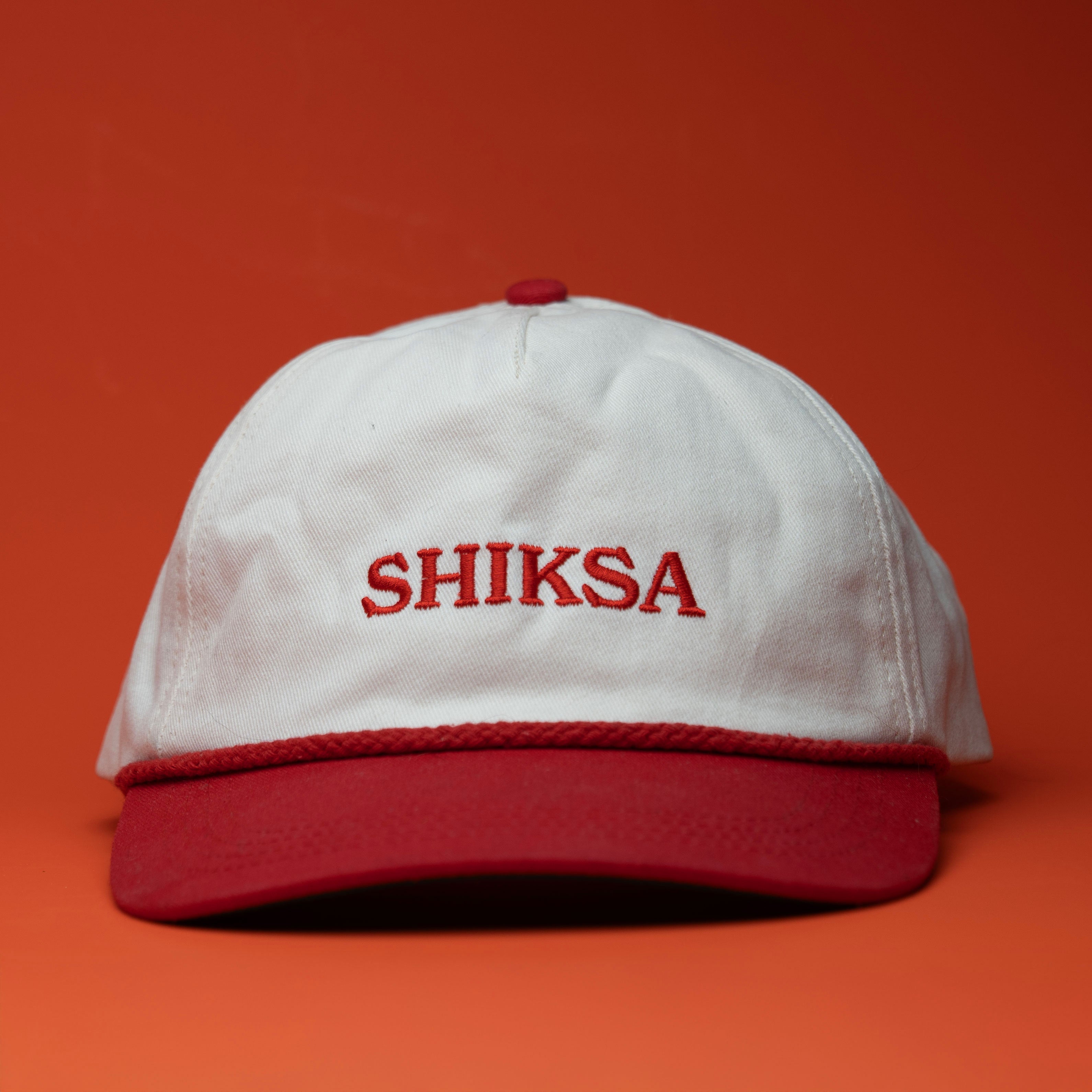 White cap with red brim and 'SHIKSA' text on a red background
