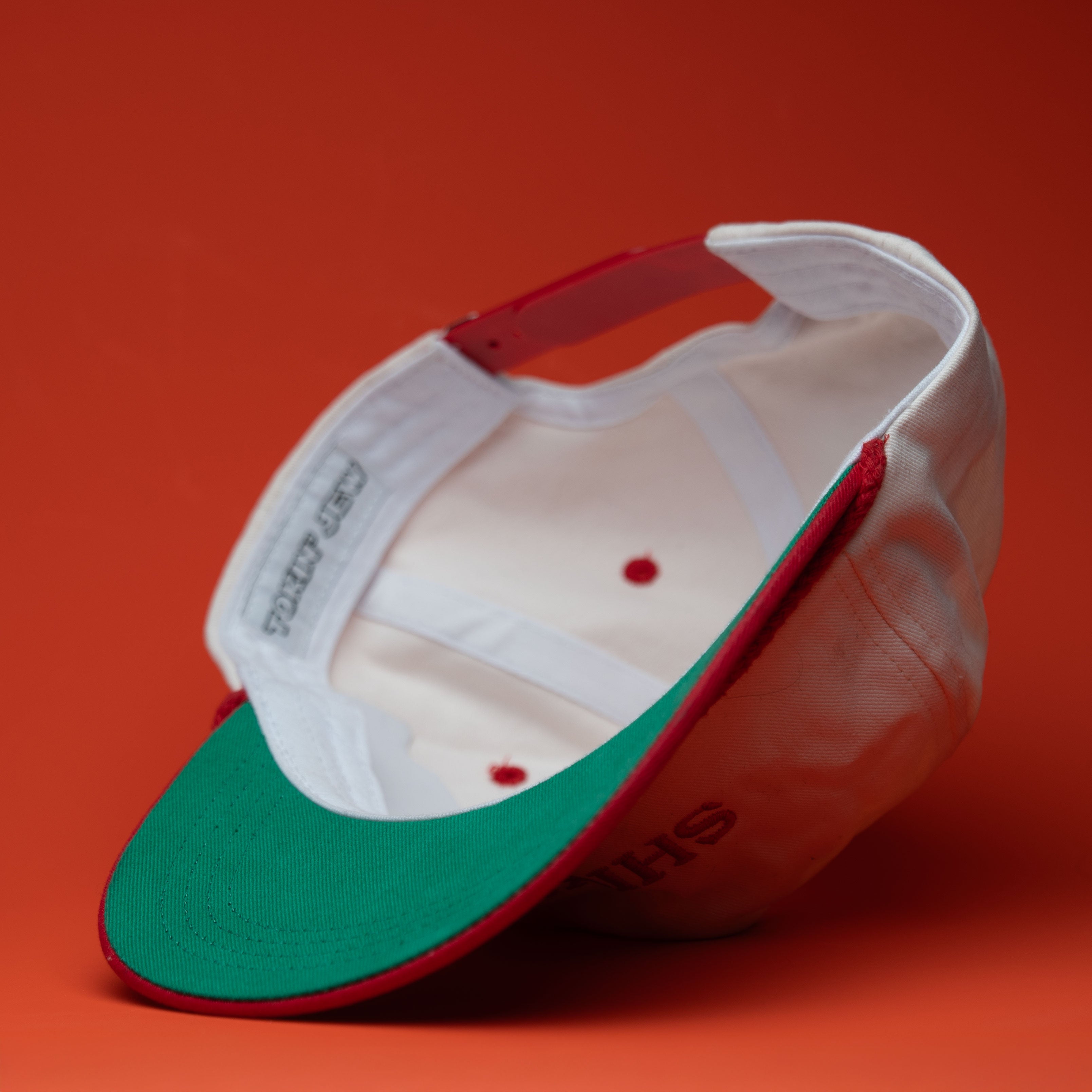 Baseball cap with green brim and red interior on a red background