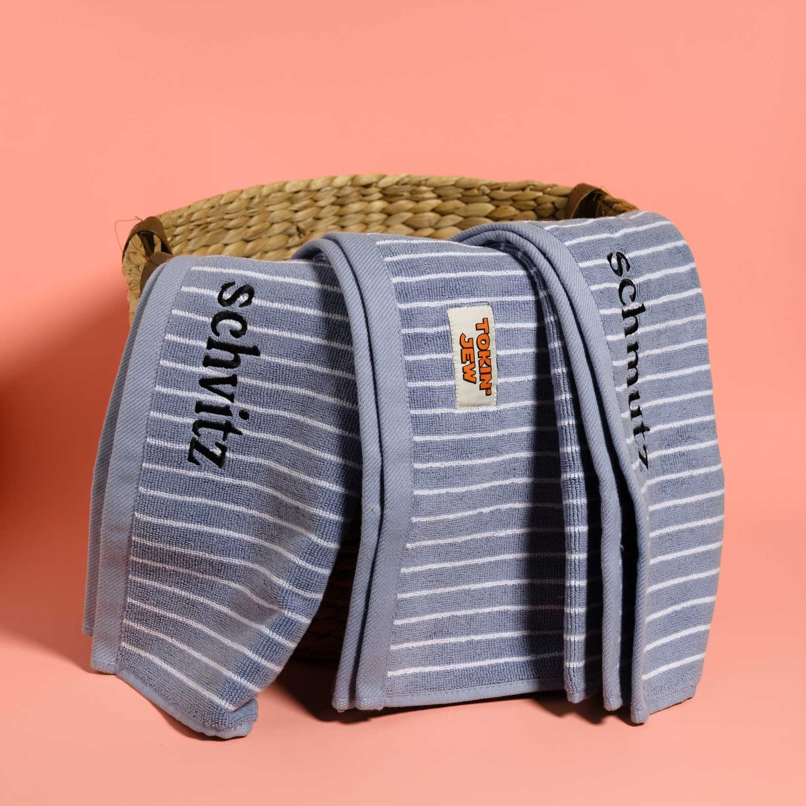 Folded blue striped towels with 'Tokin' Jew' branding on a pink background