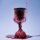 Red wine being poured into a glass kiddush cup against a blue background