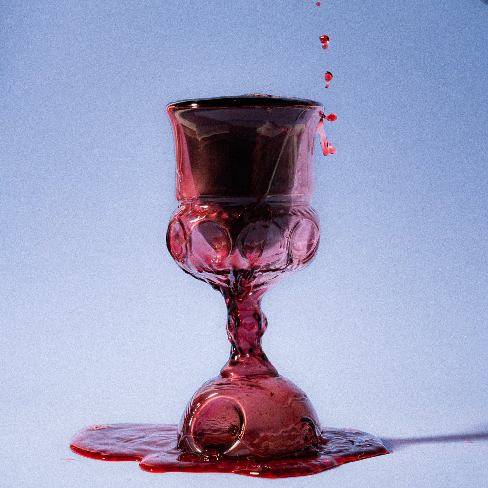 Red wine being poured into a glass kiddush cup against a blue background