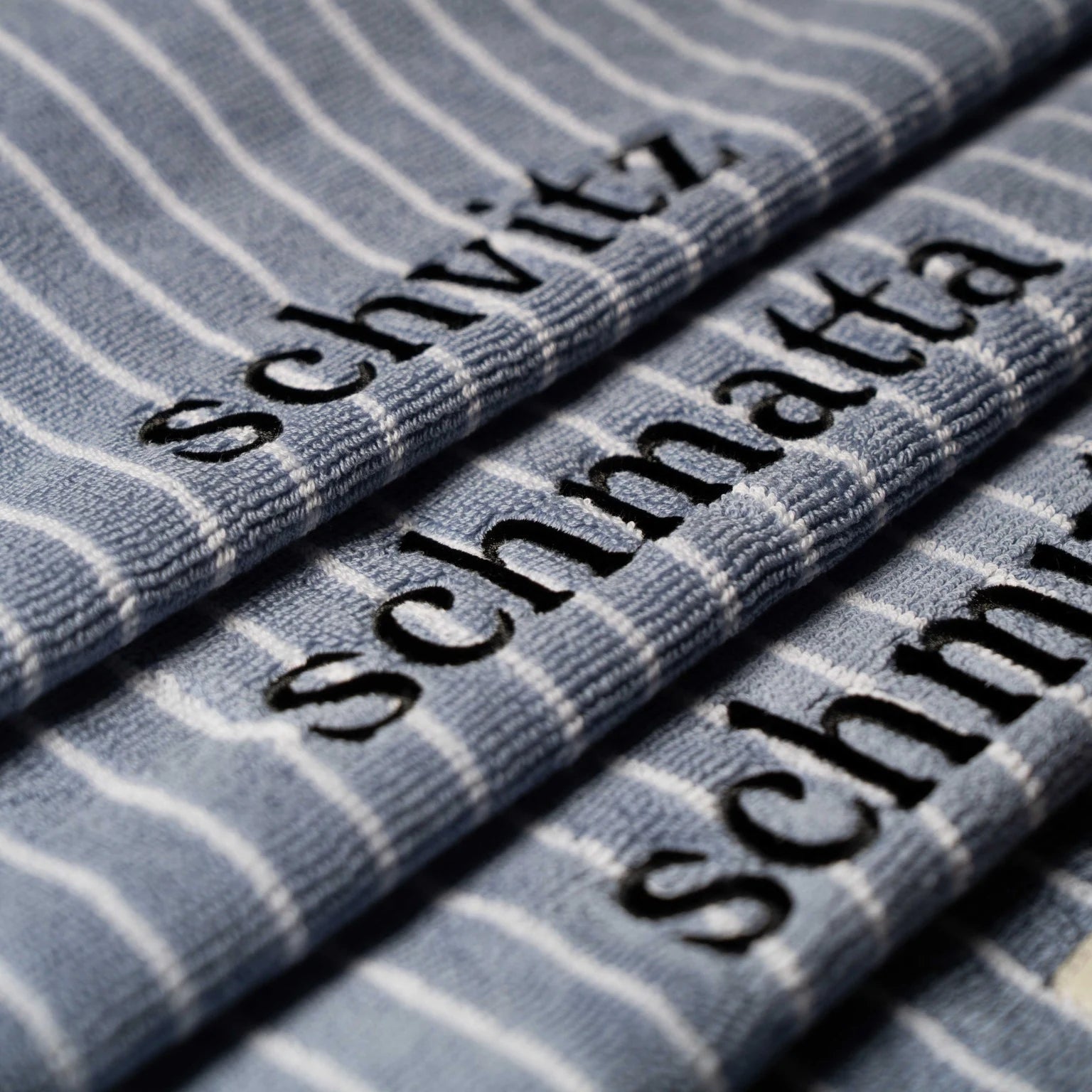 Textured towel with 'schvitz' and 'schmatta'  embroidered in black.