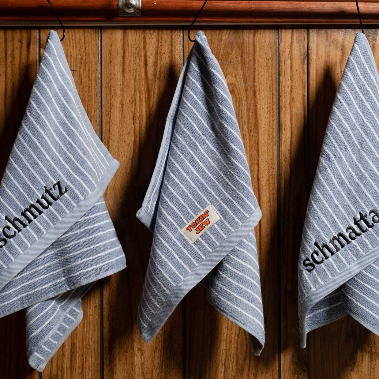 Three striped towels with 'Tokin' Jew' branding hanging on a wooden wall.