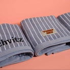 Three blue striped towels with embroidered text on a pink background
