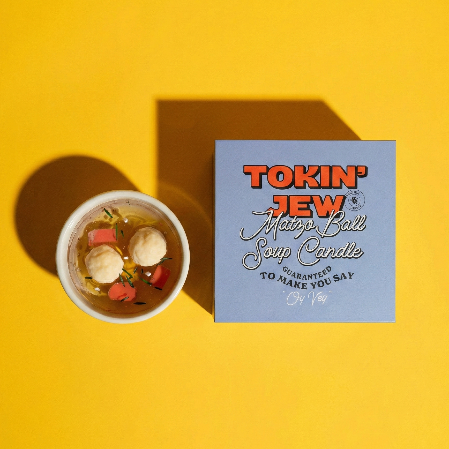 Candle with packaging labeled 'Tokin' Jew Matzo Ball Soup Candle' on a yellow background