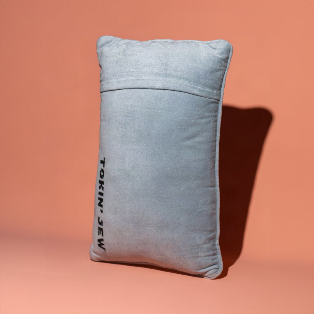 A light blue-gray rectangular throw pillow with black vertical text reading 'TOKIN' JEW' on the left side, set against a solid peach-pink background with a soft shadow.